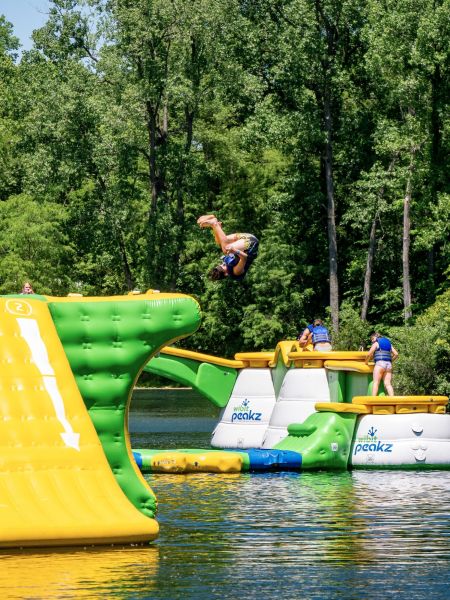 Indian Springs Campground & Water Park - Family enjoying the new Splash Springs Floating Water Park with water slide, beach area, and scenic fishing lakes in a serene forest setting. Perfect for camping, fishing, and water fun near Fort Wayne.