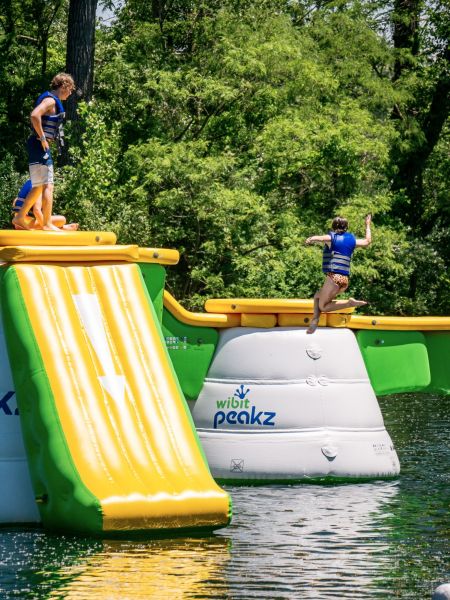 Indian Springs Campground & Water Park - Family enjoying the new Splash Springs Floating Water Park with water slide, beach area, and scenic fishing lakes in a serene forest setting. Perfect for camping, fishing, and water fun near Fort Wayne.